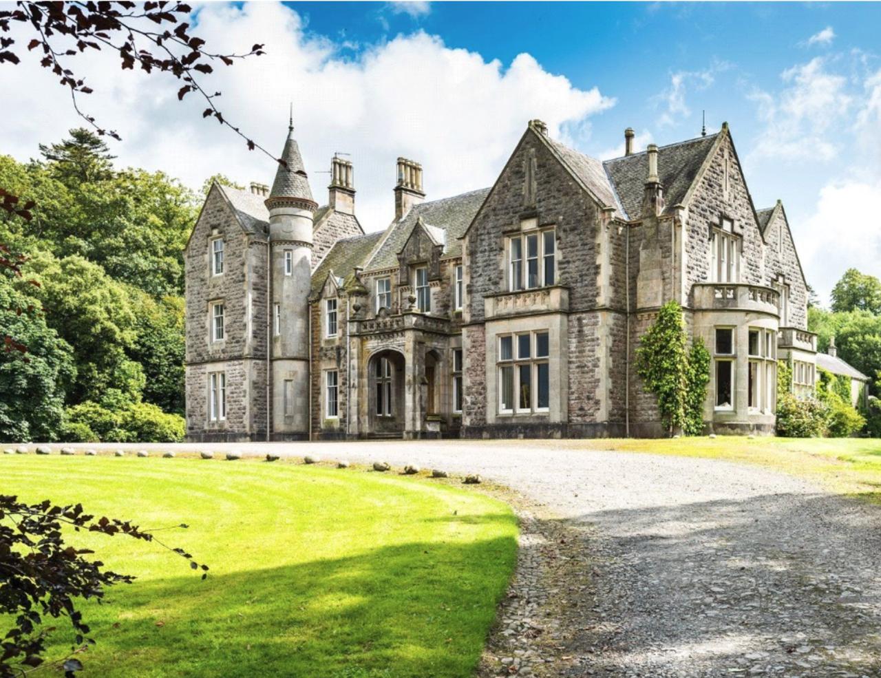 Gilford Castle, a stone Victorian castle with a turret, seen across its front lawn and gravel drive